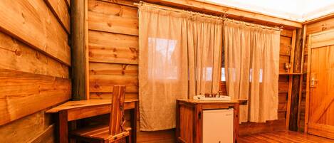 A wooden cabin interior with a wooden chair, a small table, a sink, and a door.