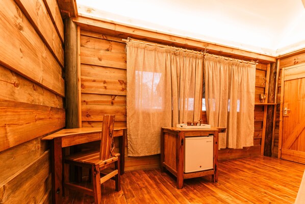 A wooden cabin interior with a wooden chair, a small table, a sink, and a door. - MISENI RETREAT (Saadani)