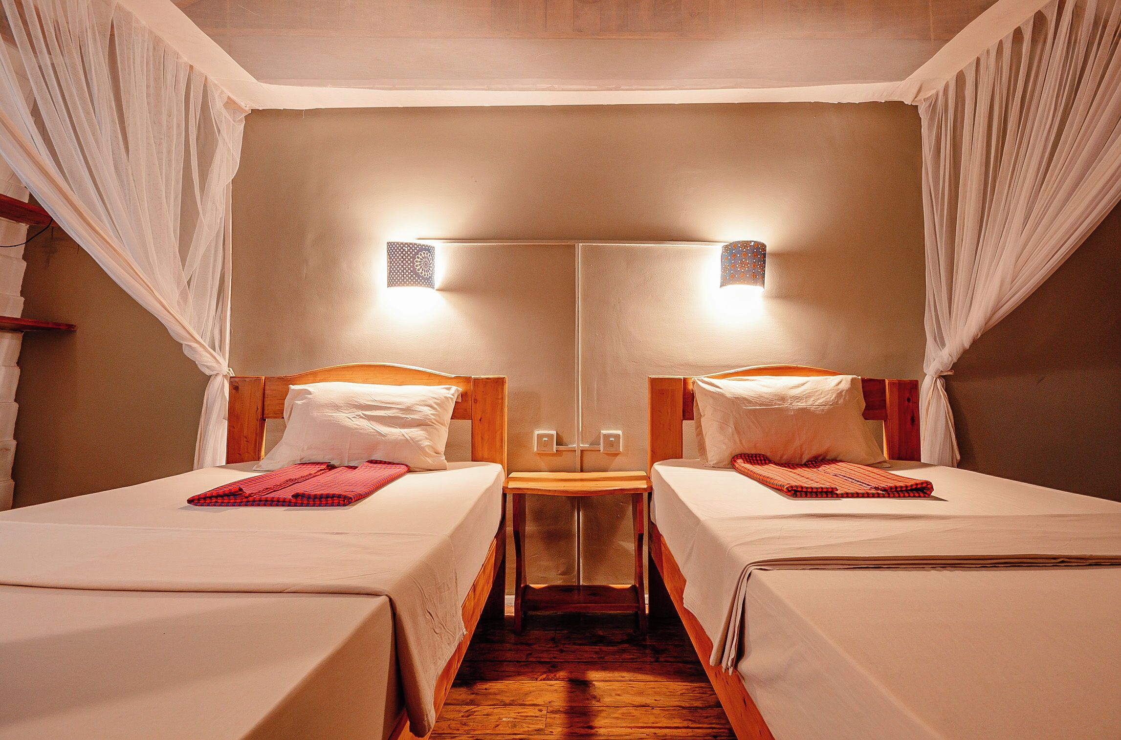A room with two beds, a wooden nightstand, and a mirror between them.