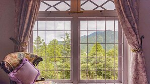 Una habitación con un ventanal grande, un sillón floral y vistas a una montaña boscosa.