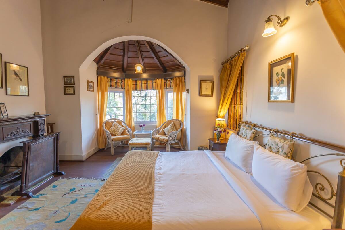 Um quarto espaçoso com uma cama grande, lareira e vista através de uma janela em arco.