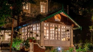 Un edificio de estilo tradicional con un porche cubierto, plantas en macetas y un muro de ladrillo.