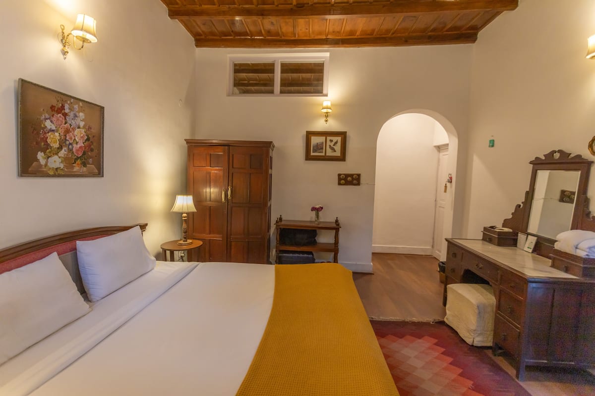 Quarto de hotel com cama, guarda-roupa de madeira, toucador com espelho e um quadro na parede.