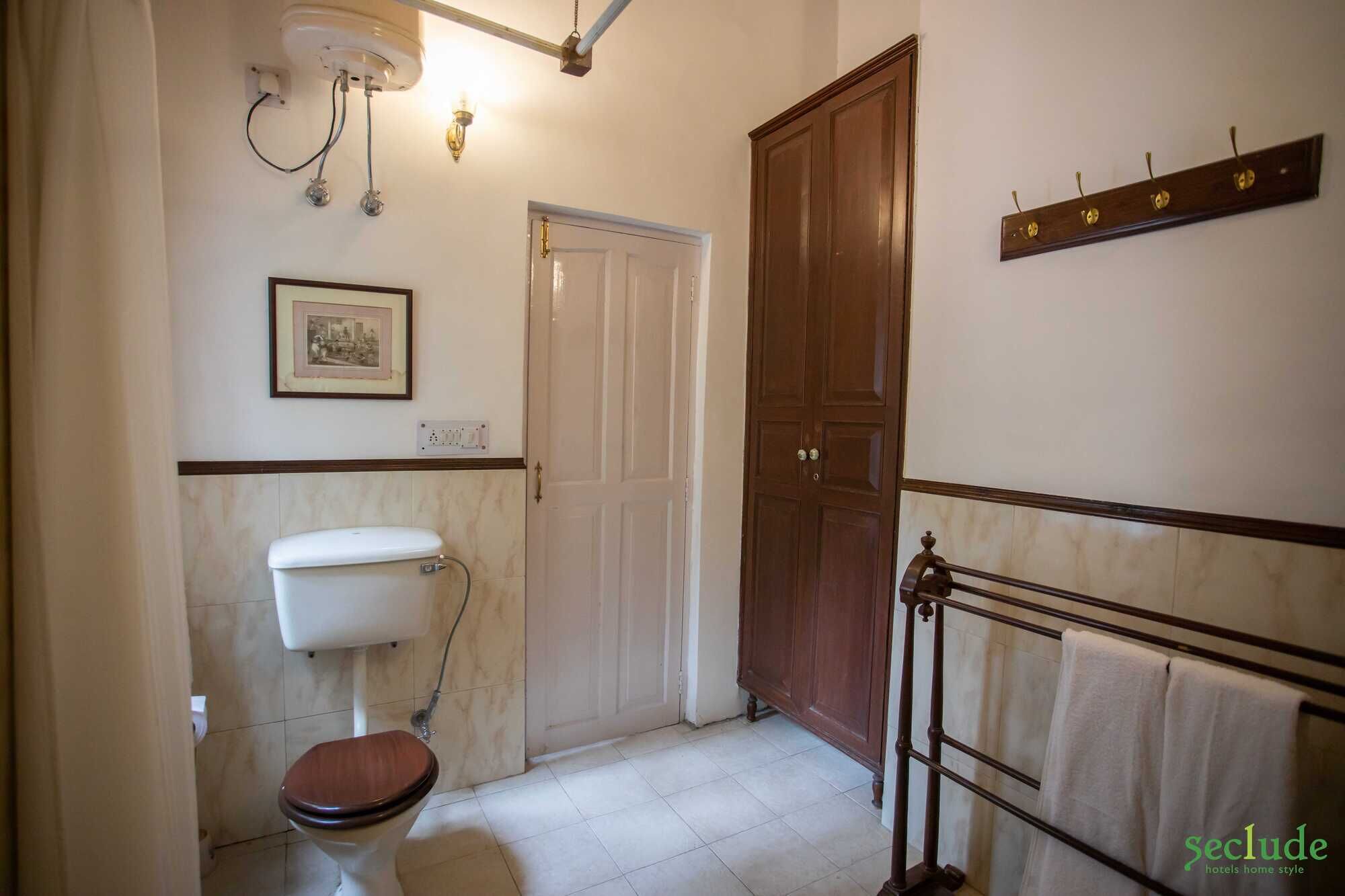 Un baño con inodoro, una puerta de madera, toallero y un accesorio de iluminación instalado en la pared.