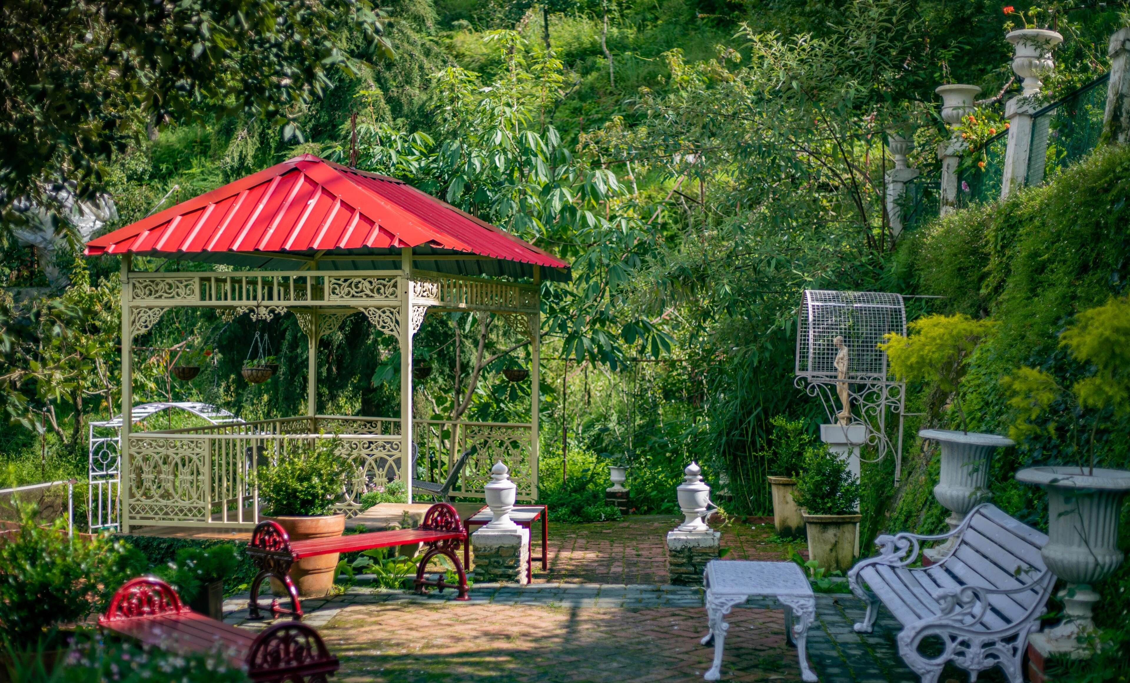 A gazebo with a red roof, surrounded by lush greenery and garden furniture.
