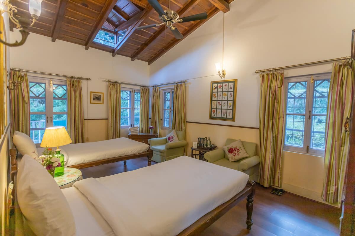 Quarto com duas camas, ventoinha no teto e janela com cortinas.