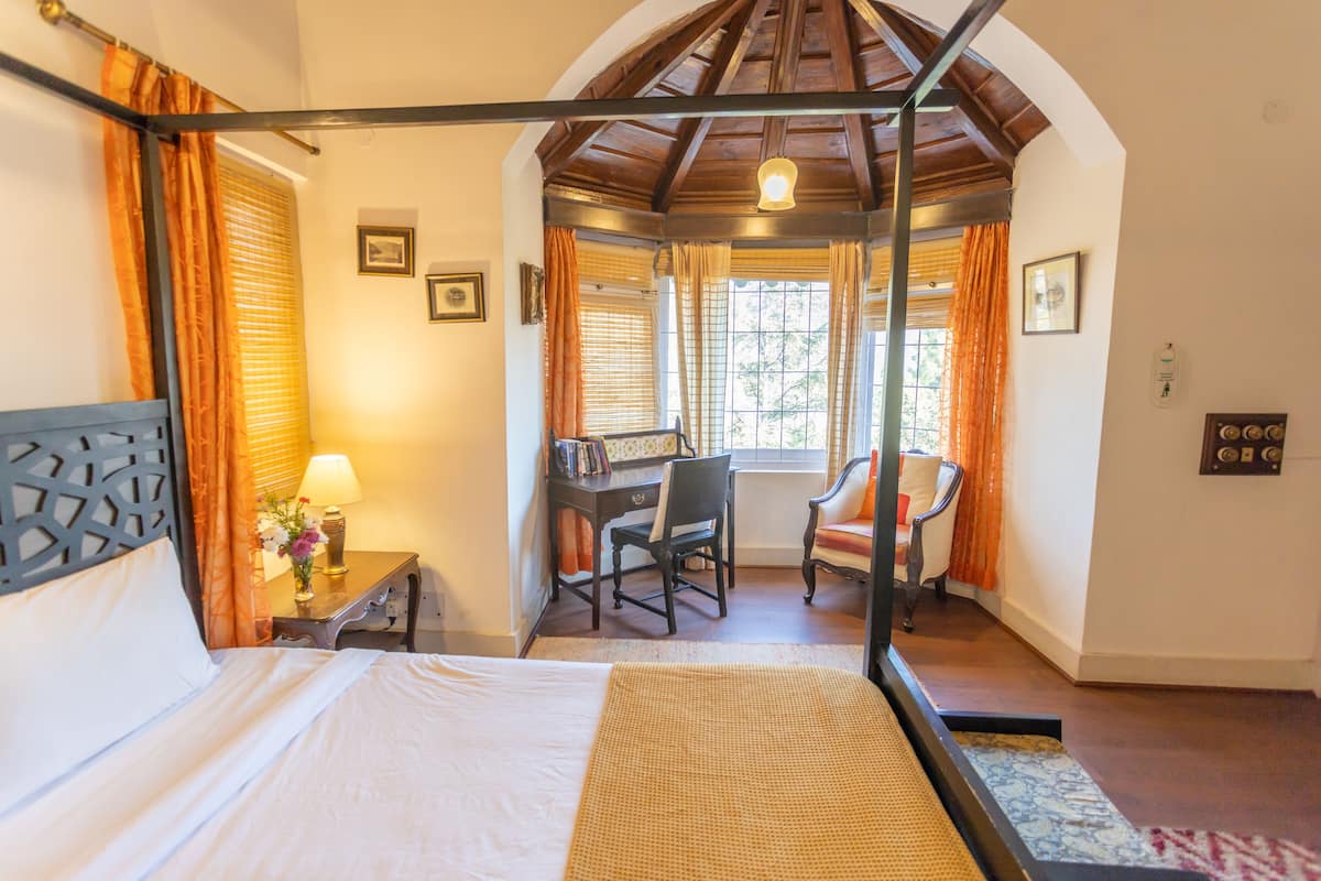 Quarto com cama de dossel, escrivaninha com cadeira e janela com cortinas.
