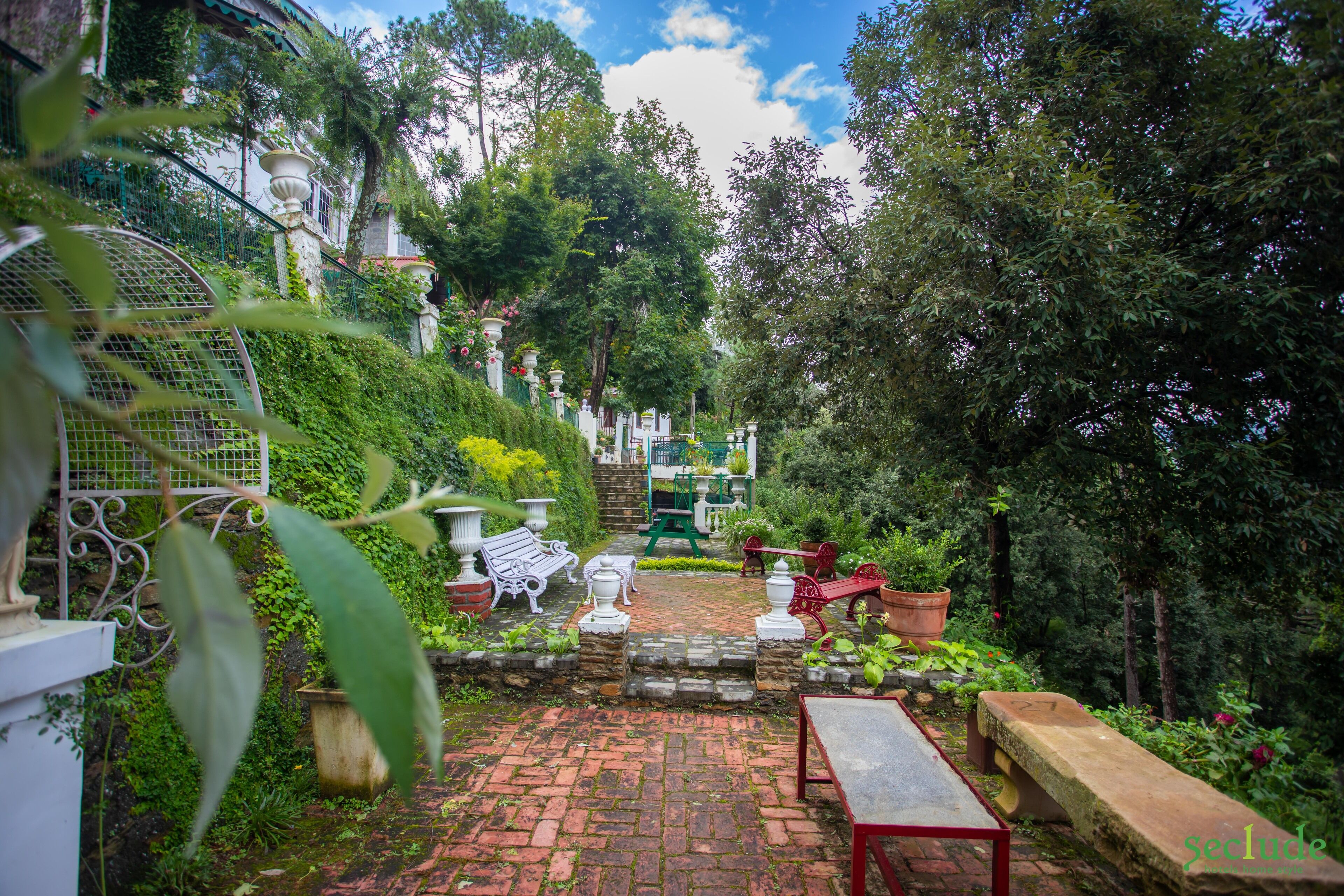 A garden with a brick pathway, benches, and potted plants.