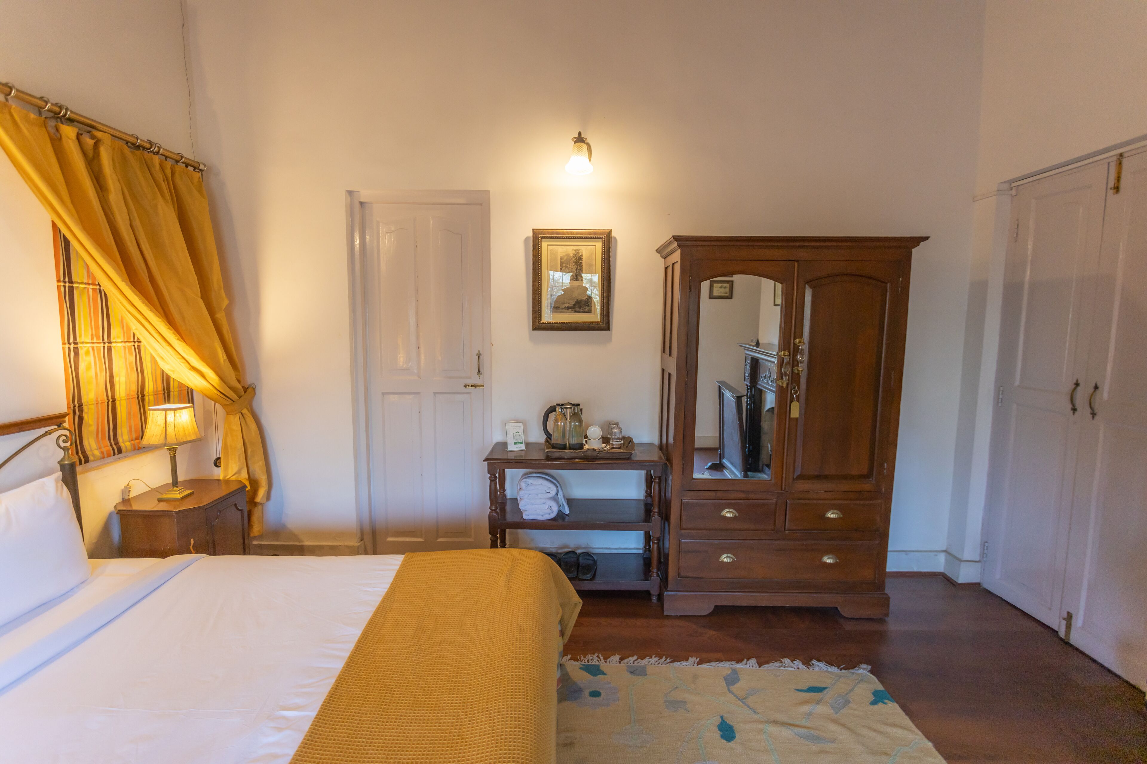 A bedroom with a bed, a nightstand, a wardrobe, a mirror, a shelf with towels, and a wall-mounted light.