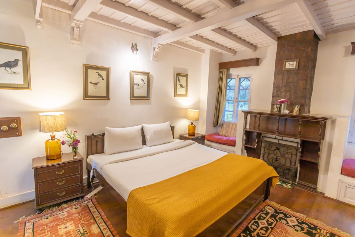 Quarto com cama, mesas de cabeceira, lareira e quadros nas paredes.