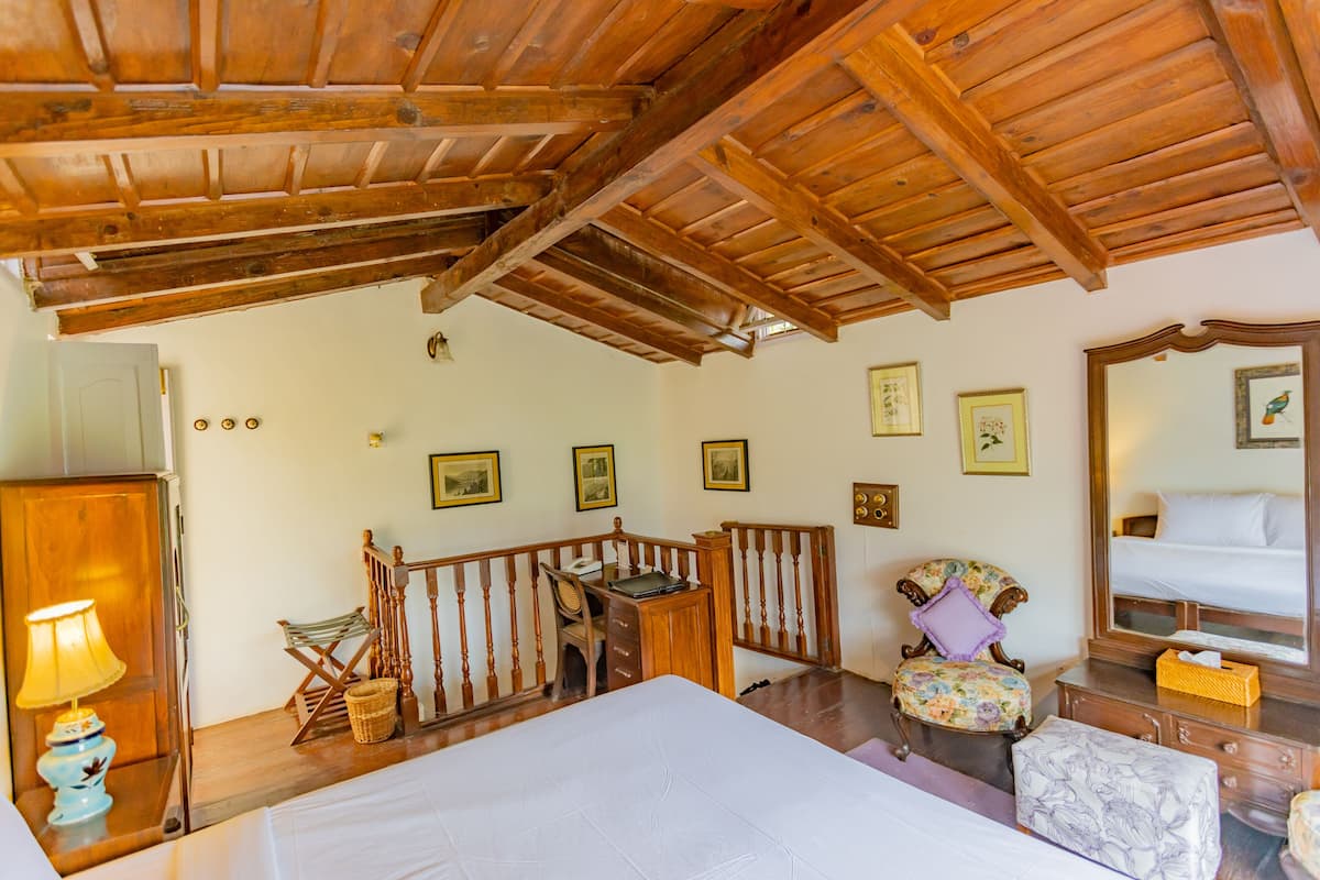 Um quarto com teto de madeira, uma cama, uma escrivaninha, uma cadeira e uma cômoda.