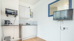 A modern kitchen with white cabinets, a microwave, a kettle, and a flat-screen TV mounted on the wall. - The Modern Cambridge Studio 4 (Cambridge)