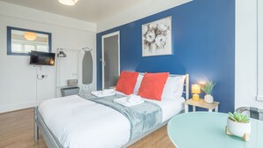A modern hotel room with a bed, a bedside table with a lamp, a small potted plant, and a wall-mounted TV. - The Modern Cambridge Studio 4 (Cambridge)