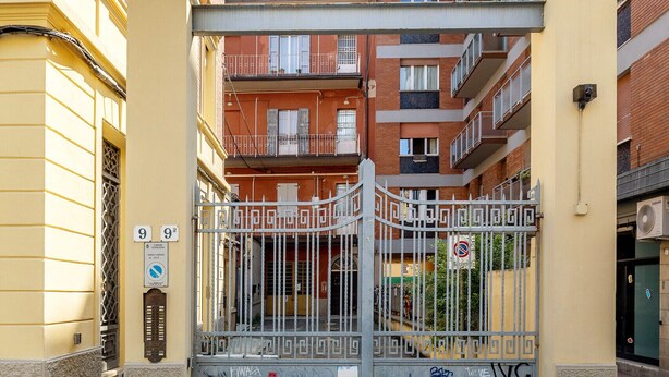 A gated entrance to a residential building with balconies, a sign indicating the entrance number, and a security camera. - Bright Studio with Balcony by Wonderful Italy (Bologna)