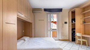 A bedroom with a bed, wooden wardrobe, and a desk with a chair. - Bright Studio with Balcony by Wonderful Italy (Bologna)