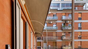 A narrow corridor with a metal railing, leading to a building entrance with a door and a window. - Bright Studio with Balcony by Wonderful Italy (Bologna)