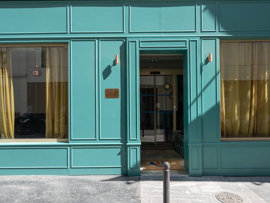Un bâtiment de couleur bleu-vert, doté de grandes fenêtres et d’une porte.