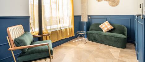 A room with a green sofa, a wooden chair, a small round table, and a wall with circular wall art.