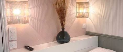 A hotel room with a bed, bedside tables, a vase with dried plants, and wall-mounted lights.