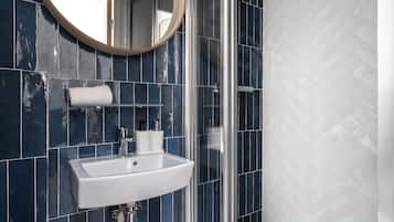 A bathroom with a white sink, dark blue tiles, a round mirror, and a towel rack.