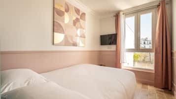 Una habitación de hotel con una cama grande, un televisor en la pared y una ventana con cortinas.