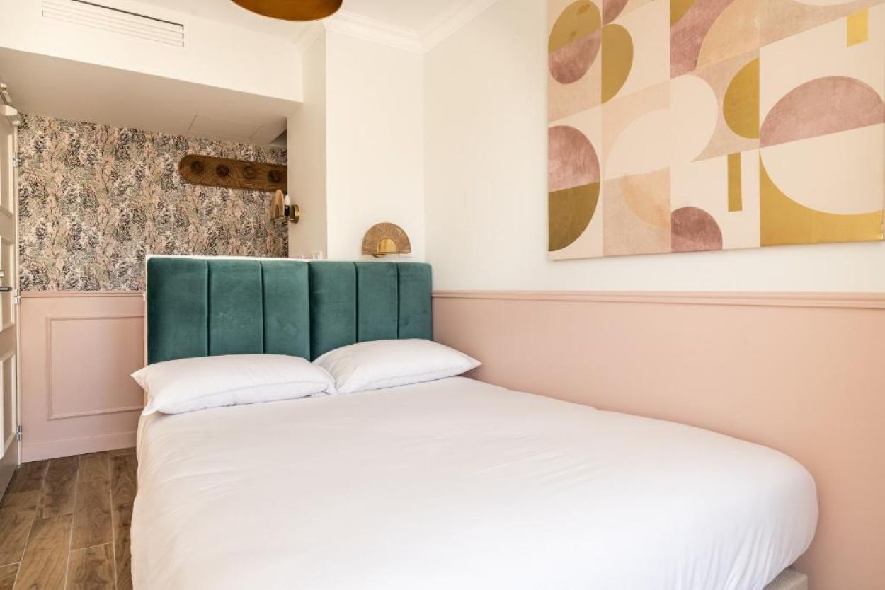 A bedroom with a teal upholstered headboard, a white bedspread, and a large abstract painting on the wall.