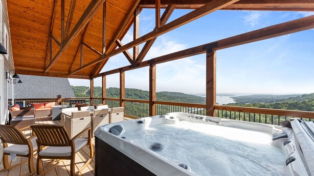 Una terraza de madera con un jacuzzi, muebles de mimbre y vistas al paisaje.