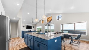 Una cocina moderna con una isla central, armarios azules y un ventanal con vistas al océano.