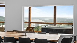 Comedor con amplia ventana con vistas a un paisaje pintoresco, jacuzzi y terraza de madera.