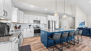 Una cocina moderna con armarios blancos, una isla azul, electrodomésticos de acero inoxidable y taburetes de bar.