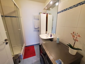 Uma casa de banho com cabine de duche em vidro, lavatório com espelho e tapete de casa de banho vermelho.