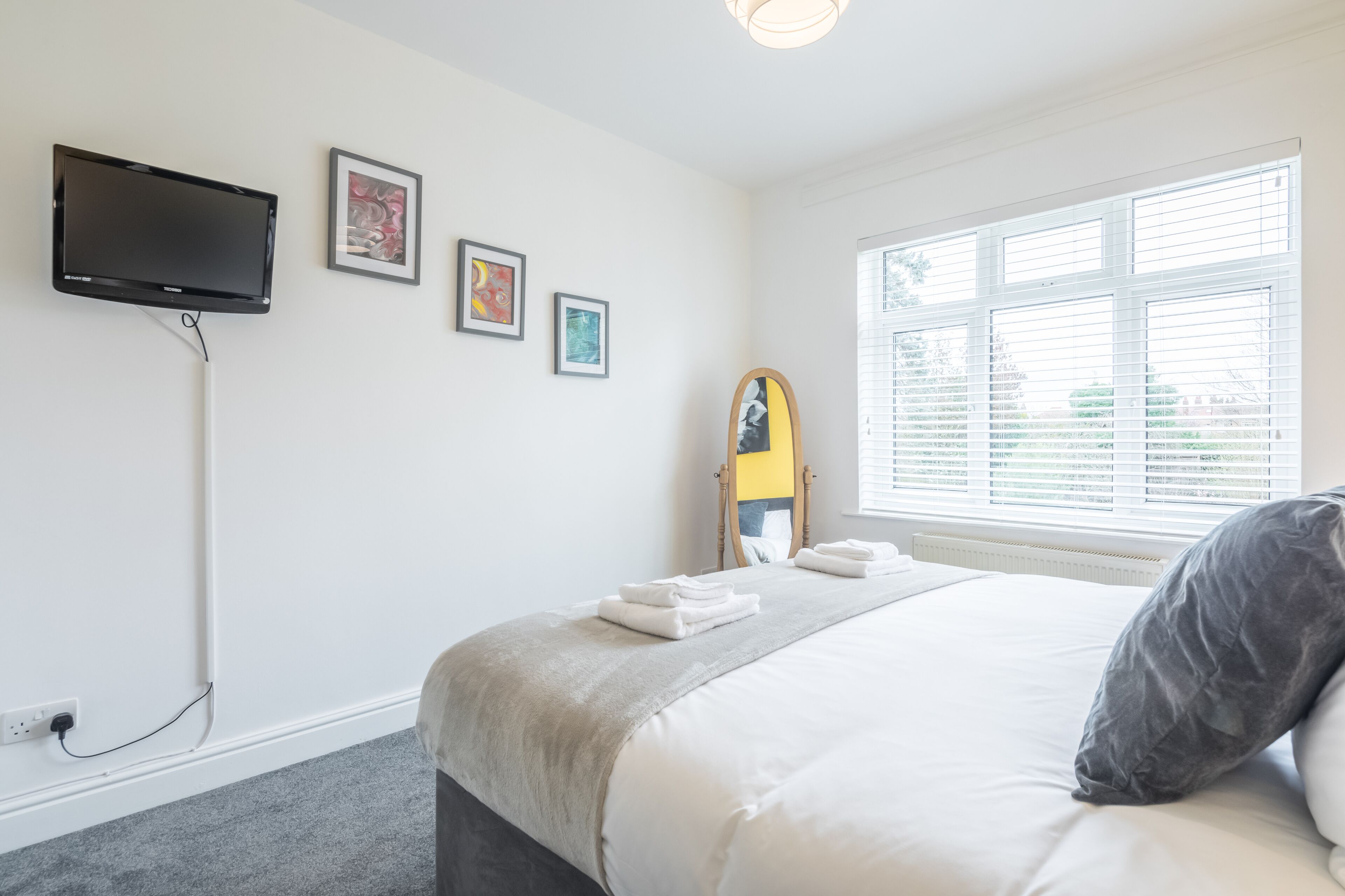 A neatly arranged hotel room with a bed, a flat-screen TV mounted on the wall, and a window with blinds.