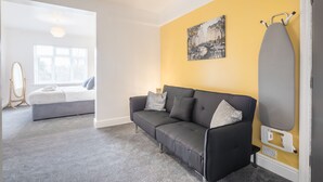 A modern living room with a grey sofa, a yellow accent wall, and a large window. - The Modern Cambridge Studio 5 (Cambridge)