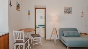 A small, well-lit room with a bed, a table with two chairs, a lamp, and a few wall decorations. - Stella Maris by Wonderful Italy (Cefalù)