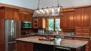 A kitchen with wooden cabinets, stainless steel appliances, a granite countertop, and a built-in dishwasher. - Timber Sky Estate - Family & Pet-Friendly Log Cabin in Elora (West Montrose)