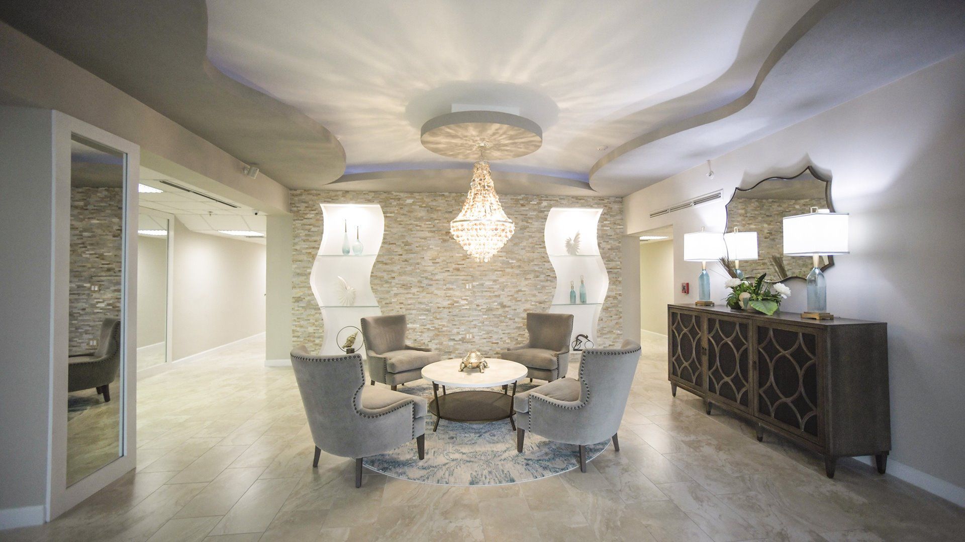 Un intérieur moderne avec une table ronde, quatre chaises, un lustre, un meuble décoratif et un mur en pierre.