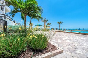 Un espace aménagé au bord de la piscine, avec une terrasse carrelée, des palmiers et une vue sur la mer.