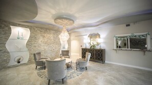 Uma sala de estar moderna com parede de destaque em pedra, um candelabro e uma mesa de centro redonda cercada por poltronas.