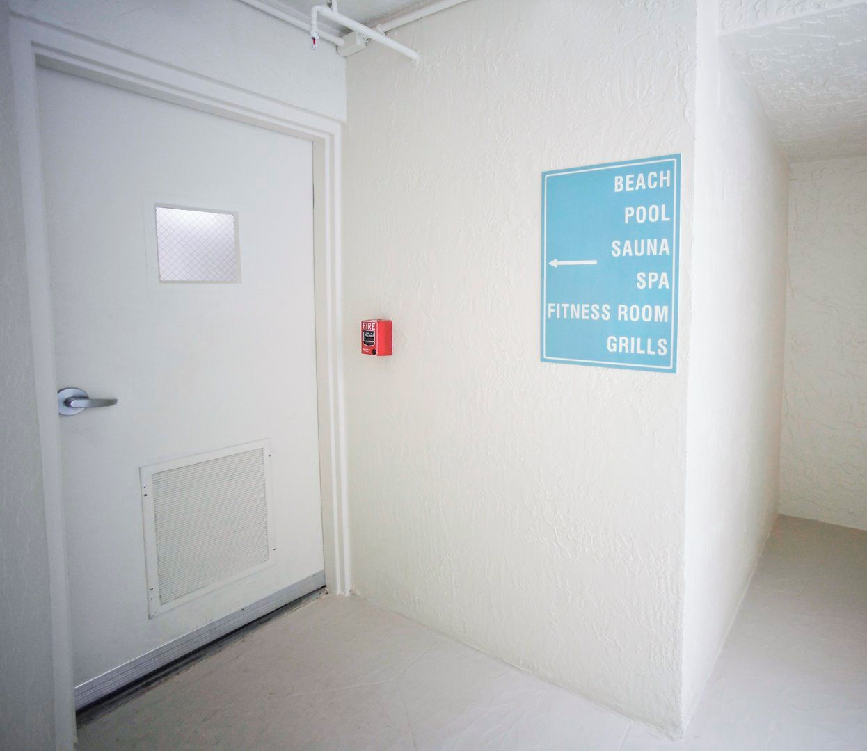 A hallway with a sign listing amenities including a beach, pool, sauna, spa, fitness room, and grills.