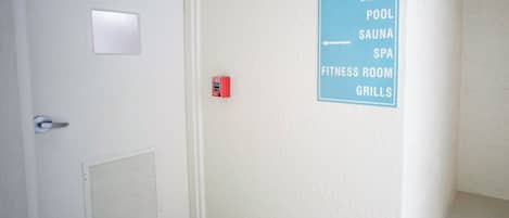 A hallway with a sign listing amenities including a beach, pool, sauna, spa, fitness room, and grills.