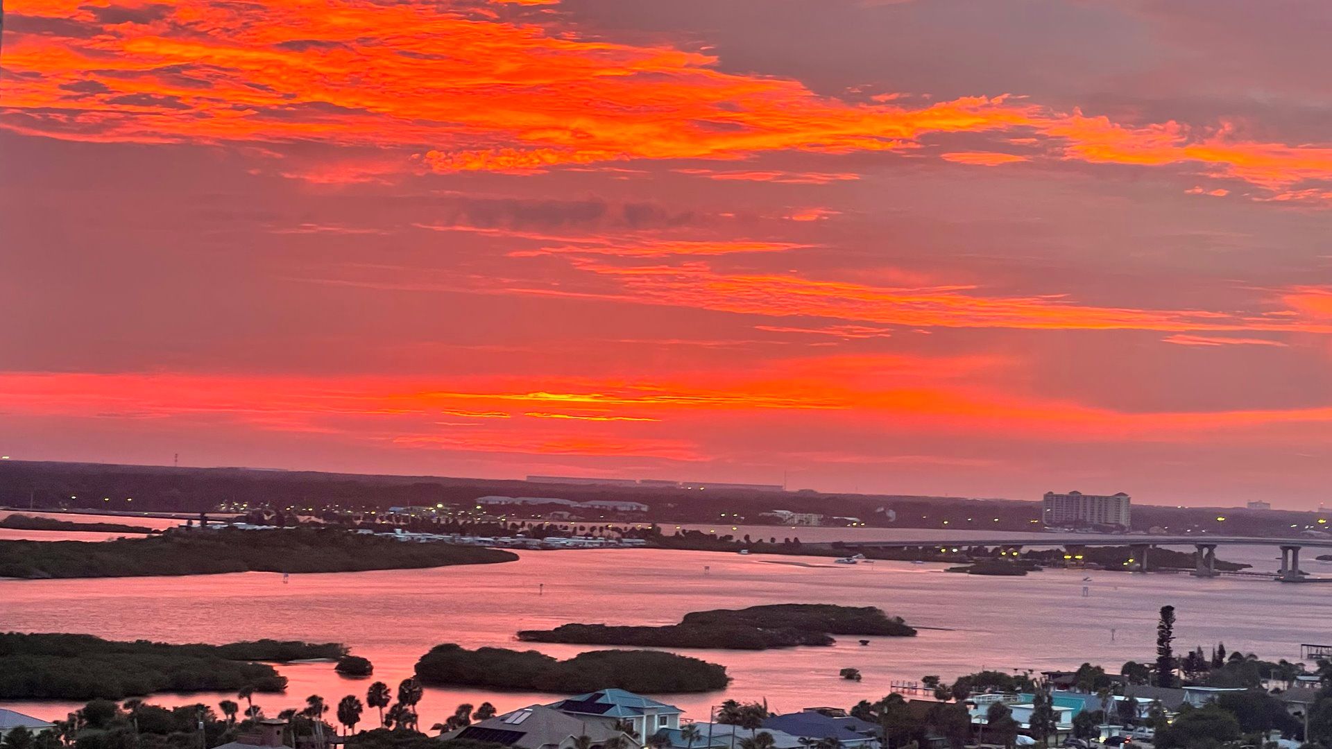 A sunset over a river with a bridge and buildings in the distance.