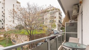 A balcony with a glass table and chairs, overlooking a street with parked cars and buildings. - Supreme Athens Home by Cloudkeys (Zografos)