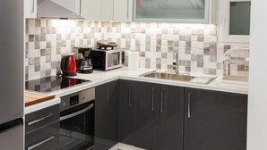 A modern kitchen with a microwave, kettle, and toaster on the countertop, a stainless steel sink, and a large window above the sink. - Supreme Athens Home by Cloudkeys (Zografos)