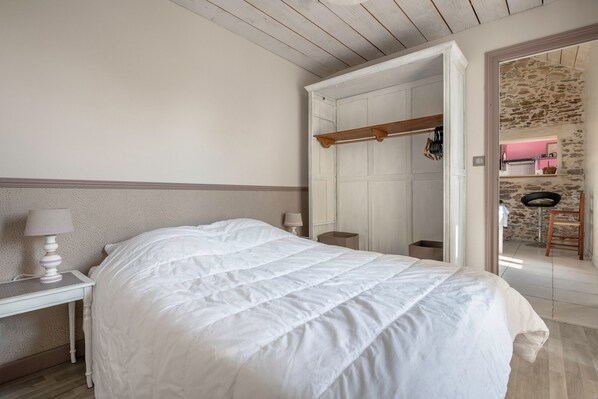 A bedroom with a bed, bedside table, lamp, and a view of a bathroom and kitchen area.