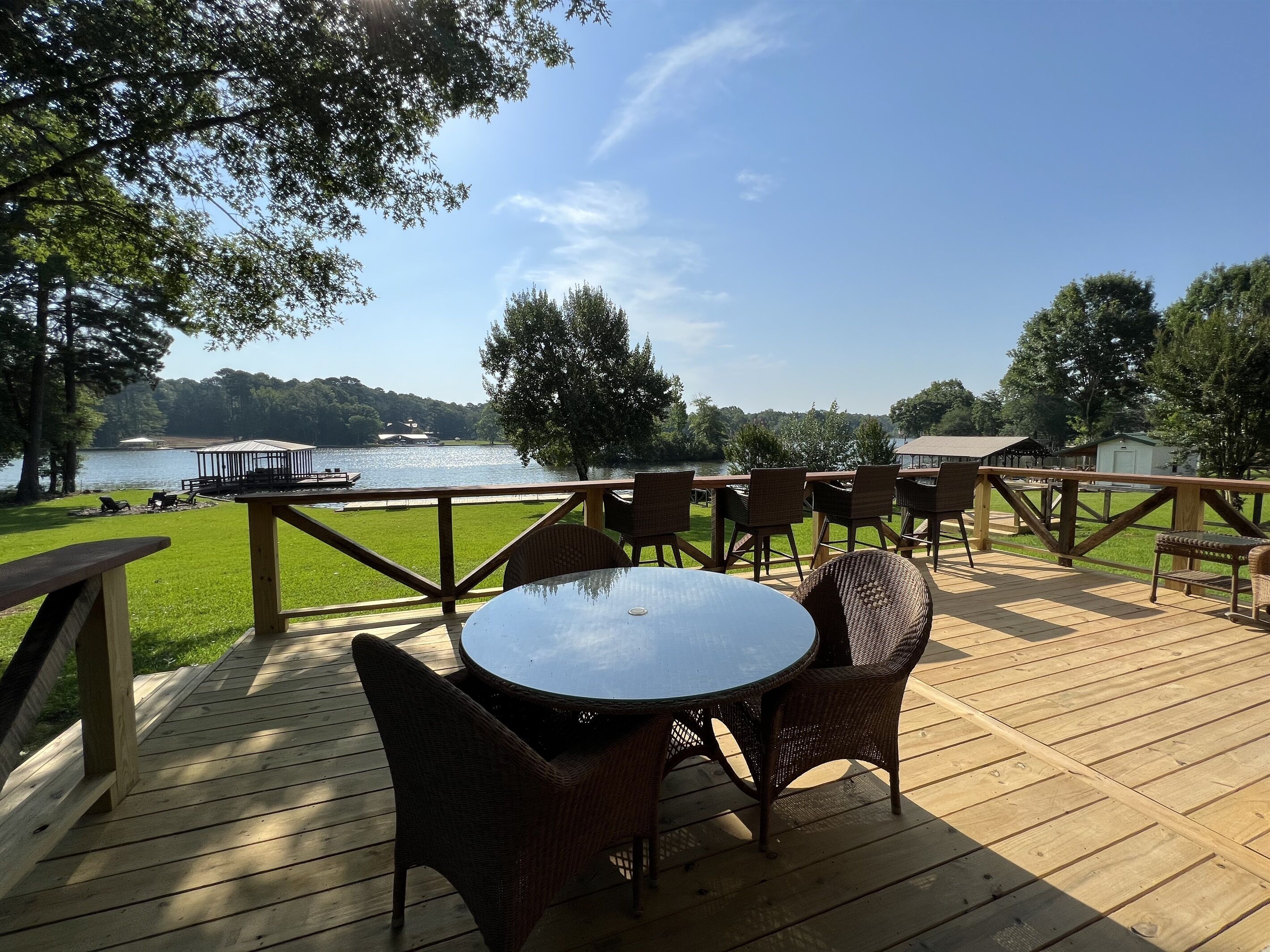 Een houten terras met rieten stoelen en een tafel, met uitzicht op een meer met boten en een prieel.