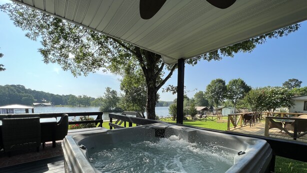 A hot tub on a wooden deck with a view of a lake and surrounding greenery. - Woodland Bungalow-Hot Tub, Boat Dock, + Game Room (Royal)