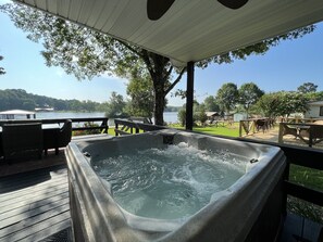 Un jacuzzi en una terraza de madera con vista a un lago y follaje circundante.