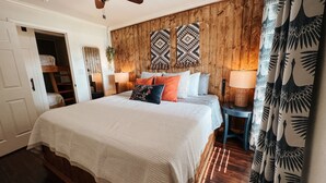 A bedroom with a large bed, wooden panel walls, a ceiling fan, and a window with curtains. - Woodland Bungalow-Hot Tub, Boat Dock, + Game Room (Royal)