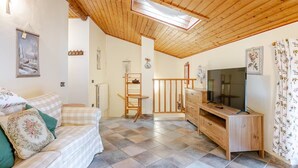 Ein gemütliches Wohnzimmer mit Holzboden, einer Couch mit gemusterten Kissen, einem Fernsehtisch und einem Essbereich mit Stuhl und Tisch.