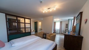 Hotellihuone, jossa on suuri sänky, peilillä varustettu työpöytä, kaksi tuolia, pieni pöytä ja näkymä käytävälle.
